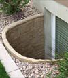 A durable plastic egress window well installed in a rock garden in Johnstown.